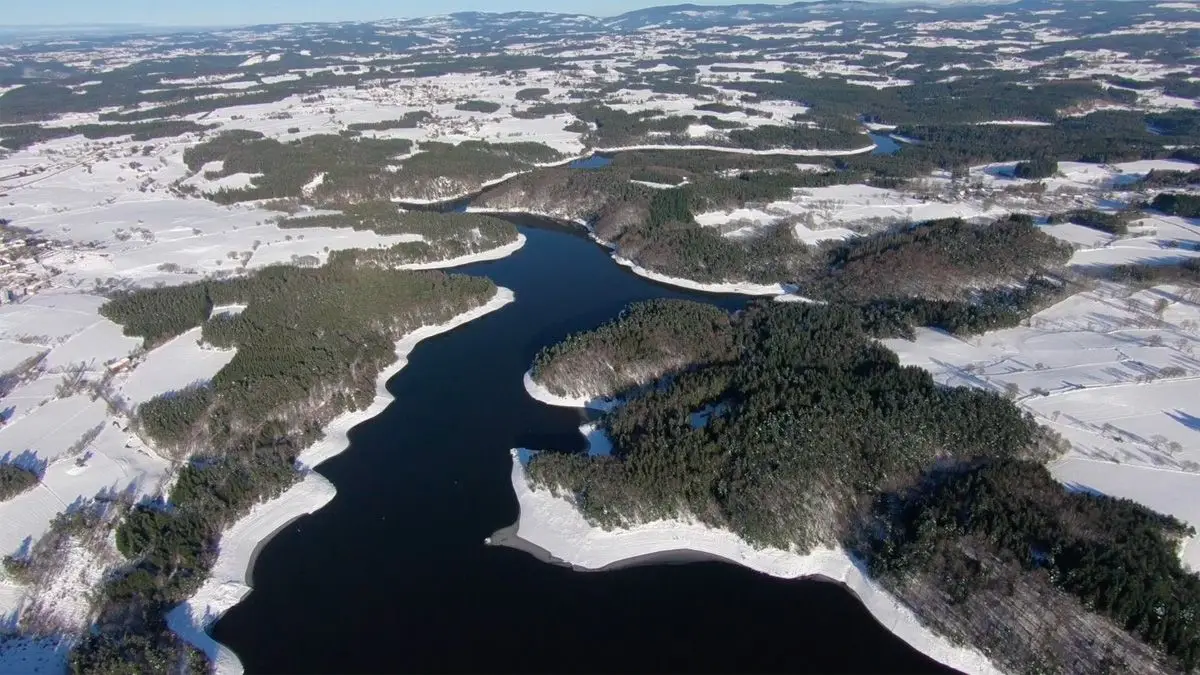 Vue aérienne d'une retenue d'eau sinueuse bordée de forêts et de champs enneigés